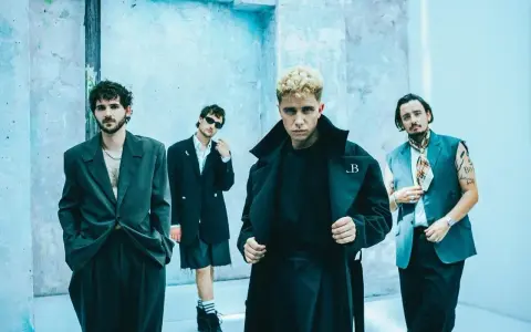 Le groupe Last Train pose devant un mur bleu clair, quatre hommes aux styles audacieux.
