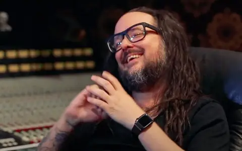 Jonathan Davis, le chanteur de Korn, rit en studio d'enregistrement, lunettes sur le nez et longue chevelure brune.