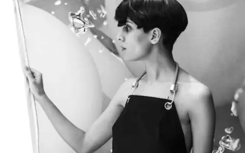 Fatima Al Qadiri, artiste à la coupe courte, porte un tablier noir, regardant une œuvre abstraite.