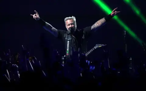 James Hetfield, un des membres de Metallica, salue la foule avec les cornes du diable, éclairé par des faisceaux verts.