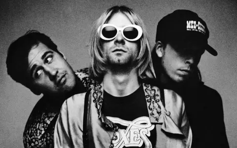 Les membres de Nirvana posent ensemble, Kurt Cobain au centre avec ses lunettes blanches iconiques.