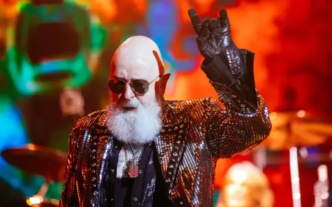 Rob Halford, un des membres de Judas Priest, fait le signe des cornes sur scène, vêtu d'une veste scintillante.