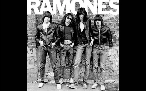 Les Ramones, quatre icônes punk en blousons de cuir et jeans, posent devant un mur de briques tagué.