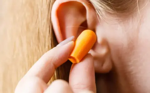 Une main insère une boule quies orange dans une oreille pour réduire les décibels.
