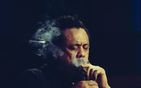 Charlie Mingus, le légendaire contrebassiste, exhale une fumée épaisse, les yeux clos, absorbé par sa musique.