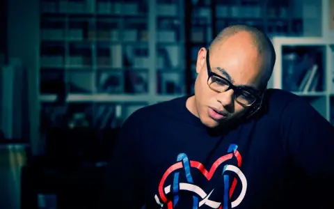 Un homme chauve avec des lunettes, parlant au téléphone, porte un t-shirt avec un logo coloré. Il pourrait bien être celui qui a inventé le rap.