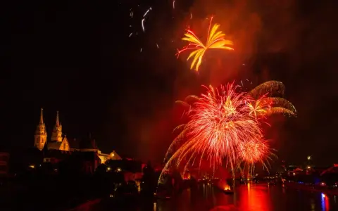 Feu d'artifice rougeoyant illuminant le ciel nocturne au-dessus d'une ville et d'une rivière. Le **décibel feu d'artifice** résonne dans l'air.