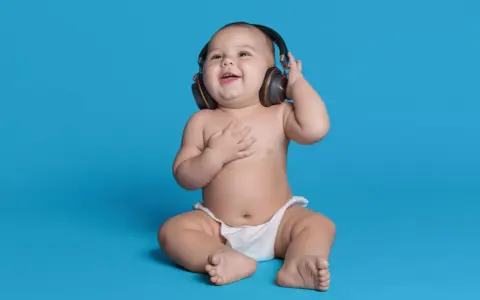 Un bébé souriant, en couche, écoute de la musique avec des écouteurs, le décibel maximum pour un bébé est à éviter.