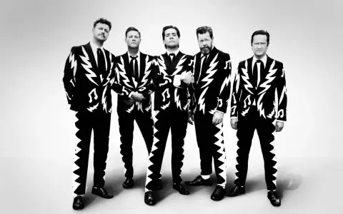 Les membres de The Hives posent en costumes noirs et blancs à motifs d'éclairs et de notes de musique.