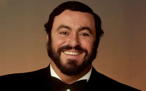 Portrait souriant de Luciano Pavarotti, le célèbre chanteur rock italien, en costume noir et nœud papillon.