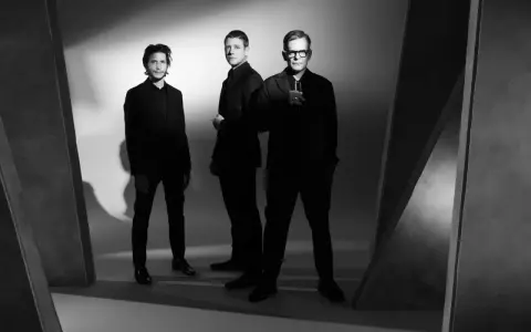 Le groupe Interpol pose en noir et blanc, trois hommes en costumes sombres, dans une ambiance épurée et artistique.