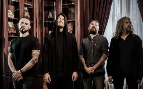 Quatre musiciens, dont un avec une capuche, posent devant des étagères remplies de livres. Ce groupe metal français connu dégage une aura mystérieuse.
