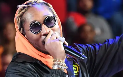Un rappeur à la mode, avec des lunettes stylées et de nombreux bijoux, chante sur scène.
