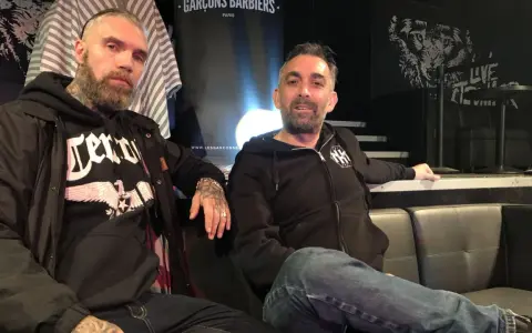 Deux hommes, dont un possible chanteur de Mass Hysteria, posent sur un canapé. L'un porte un sweat à capuche noir avec un aigle.