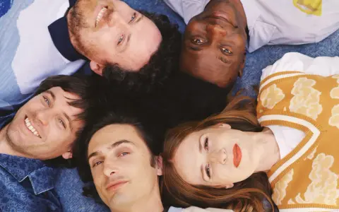 Les membres de Metronomy, cinq visages souriants, forment une étoile sur un fond bleu.