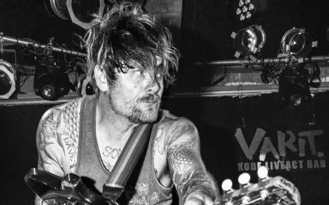 Un guitariste tatoué, cheveux en bataille, sous les projecteurs du VART. Kobe Liveact Bar.