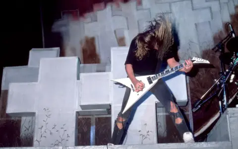 Guitariste aux cheveux longs, en plein solo, tel un maître des marionnettes sur scène.