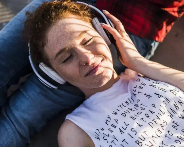 Jeune femme aux taches de rousseur, écouteurs blancs, profitant de la musique. Le volume est à 95 db équivalent, elle semble détendue.