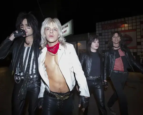 Quatre membres du groupe Motley Crue, vêtus de cuir noir et de maquillage, marchent dans la nuit.
