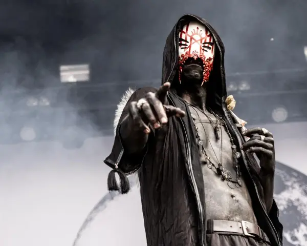 Un membre d'un groupe metal masqué, le visage peint de rouge et blanc, pointe du doigt.