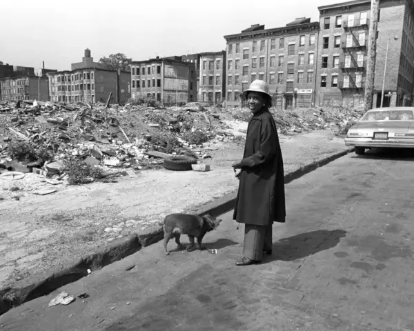 Une femme et son chien devant des immeubles délabrés et des décombres.