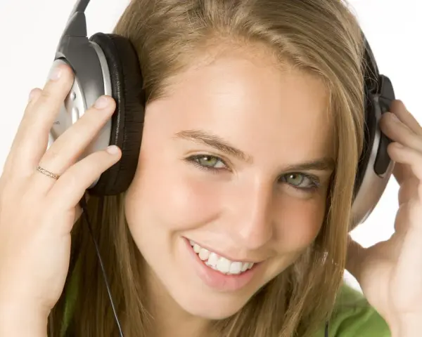 Jeune femme souriante avec des écouteurs, profitant de sa musique à 110 décibels.