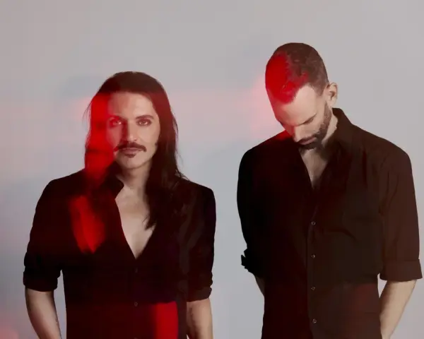 Les membres de Placebo, Brian Molko et Stefan Olsdal, posent en noir et blanc avec des éclats de lumière rouge.