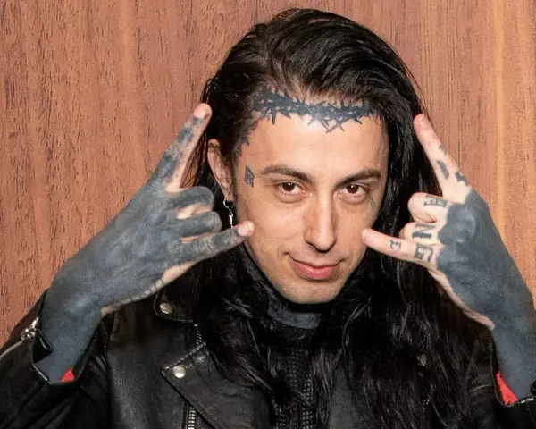 Un membre de Falling In Reverse, avec des tatouages sur le visage et les mains, fait le signe des cornes.