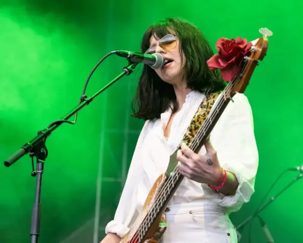 La chanteuse des Pixies, Kim Deal, joue de la basse sur scène, éclairée par une lumière verte.