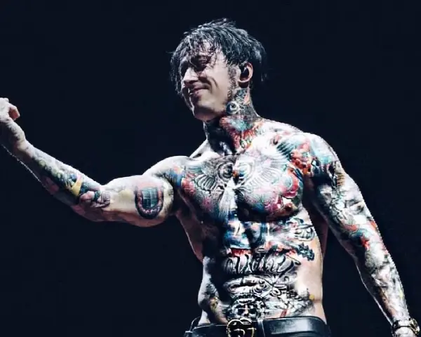 Le chanteur de Falling In Reverse, Ronnie Radke, torse nu et couvert de tatouages colorés, lève le majeur sur scène.