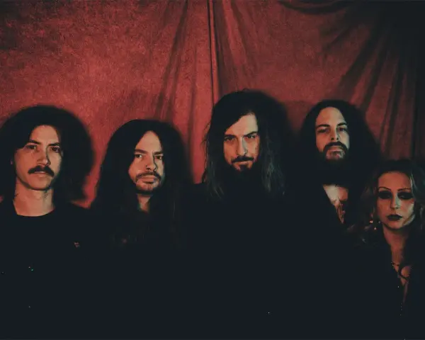 Cinq membres du groupe Uncle Acid and the Deadbeats posent devant un rideau rouge.