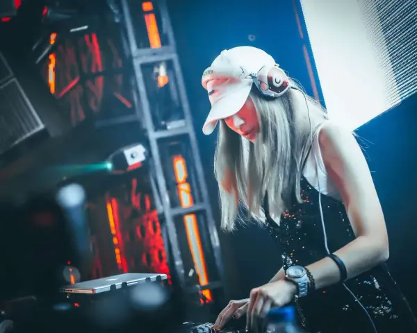 Une dj femme, casquette blanche et casque sur les oreilles, mixe dans une ambiance lumineuse et électrique.