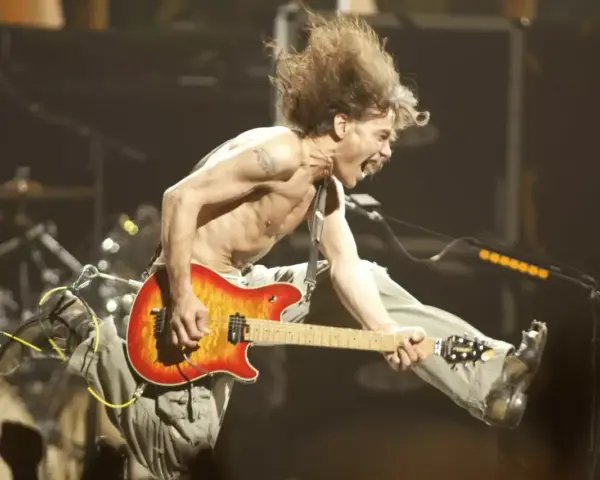 Un guitariste en plein saut, cheveux au vent, déchaîne sa guitare. Un vrai héros de la guitare en pleine action.