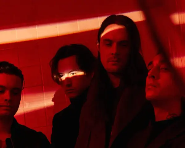 Les membres de Bad Omens posent dans une ambiance rouge intense, éclairés par des ombres dramatiques.