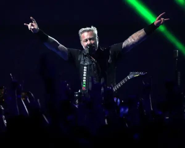 James Hetfield, un des membres de Metallica, salue la foule avec les cornes du diable, éclairé par des faisceaux verts.