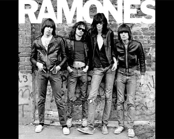 Les Ramones, quatre icônes punk en blousons de cuir et jeans, posent devant un mur de briques tagué.