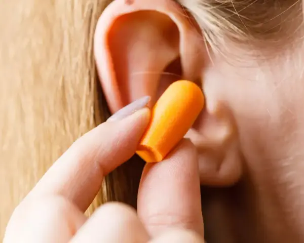 Une main insère une boule quies orange dans une oreille pour réduire les décibels.