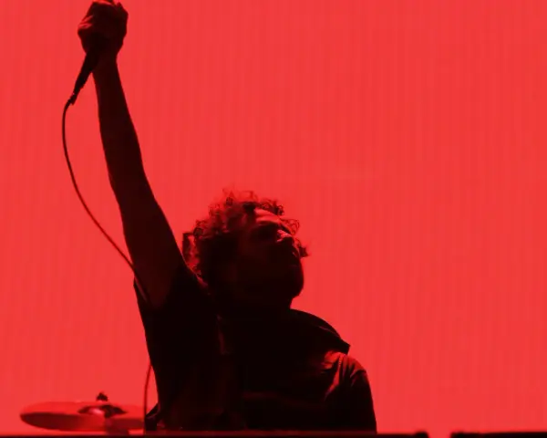 Chanteur de Rage Against the Machine, micro levé, sur fond rouge vif. L'énergie de leurs albums en live.