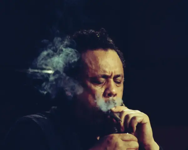 Charlie Mingus, le légendaire contrebassiste, exhale une fumée épaisse, les yeux clos, absorbé par sa musique.