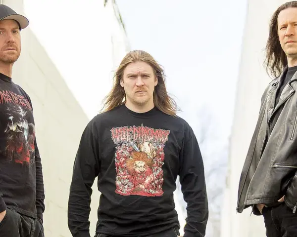 Trois hommes posent devant un mur. L'un porte un t-shirt avec une image de fœtus mourant.