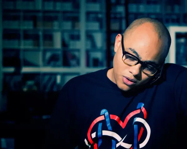 Un homme chauve avec des lunettes, parlant au téléphone, porte un t-shirt avec un logo coloré. Il pourrait bien être celui qui a inventé le rap.