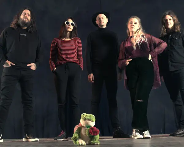 Cinq personnes se tiennent devant un fond sombre. Au premier plan, une grenouille en peluche tient une rose. Le groupe, comme un **crippled black phoenix**, semble prêt à s'envoler.