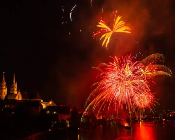 Feu d'artifice rougeoyant illuminant le ciel nocturne au-dessus d'une ville et d'une rivière. Le **décibel feu d'artifice** résonne dans l'air.