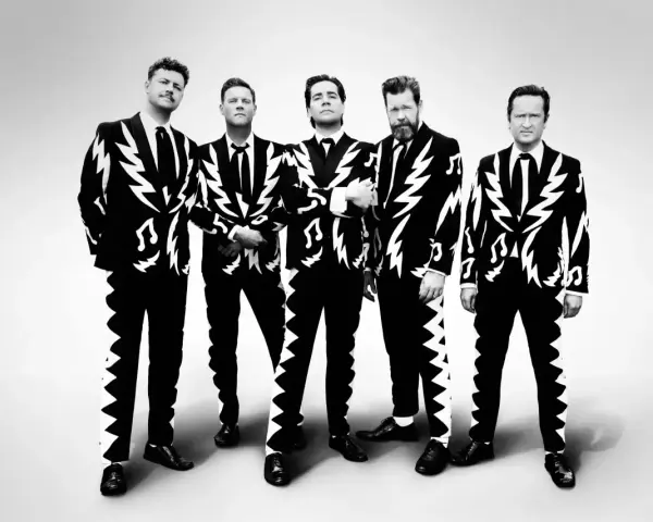 Les membres de The Hives posent en costumes noirs et blancs à motifs d'éclairs et de notes de musique.