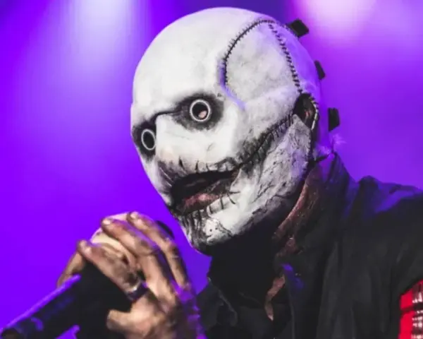 Le chanteur Slipknot, masqué et terrifiant, tient un micro sur scène sous une lumière violette.