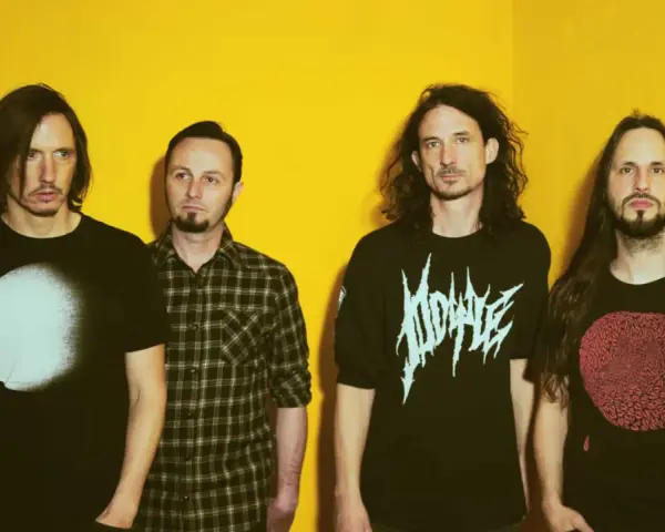 Quatre hommes aux cheveux longs posent devant un fond jaune vif. Leurs t-shirts portent des graphismes distinctifs, évoquant l'énergie brute du magma et la puissance de Gojira.