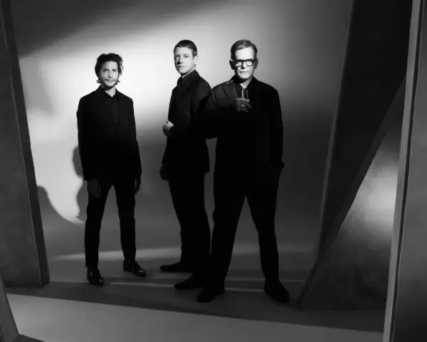 Le groupe Interpol pose en noir et blanc, trois hommes en costumes sombres, dans une ambiance épurée et artistique.