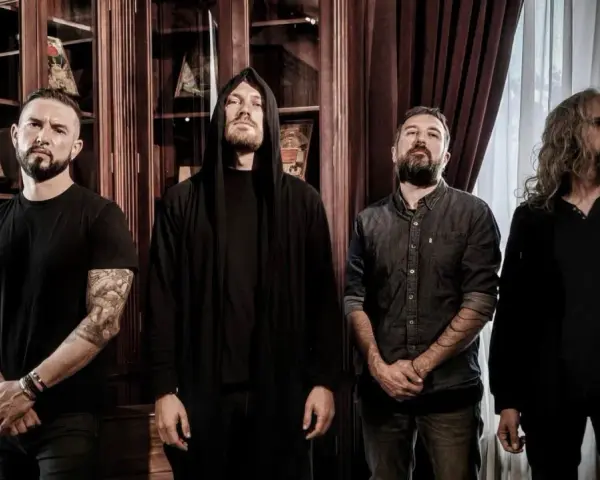 Quatre musiciens, dont un avec une capuche, posent devant des étagères remplies de livres. Ce groupe metal français connu dégage une aura mystérieuse.