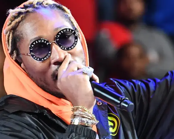 Un rappeur à la mode, avec des lunettes stylées et de nombreux bijoux, chante sur scène.