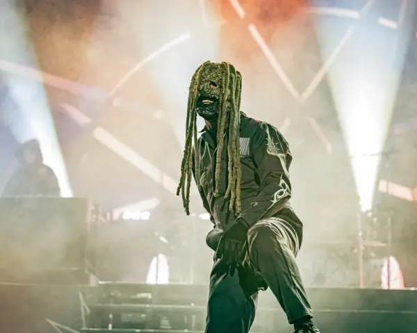Un membre de Slipknot, masqué et en combinaison, sur scène sous des projecteurs.